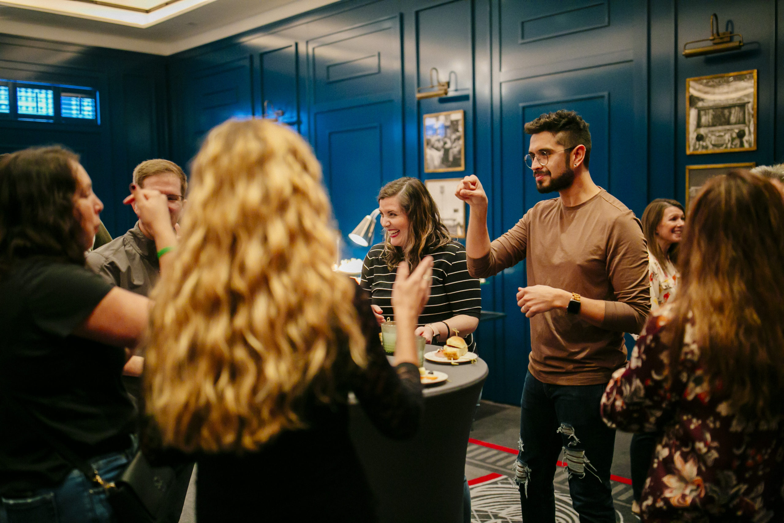 A group of people gather around a tall table at an event, conversing in American Sign Language and smiling as they share food and drinks.