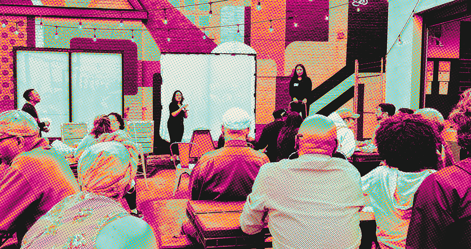 A group of people seated outdoors watching a presentation. One woman stands and signs in ASL while another stands beside her. The audience faces a colorful mural wall with string lights above.