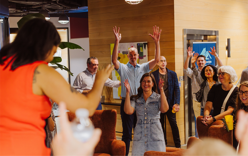 Gathering of people at an Deaf Organizations fund event cheering in ASL with arms and hands waving in the air.